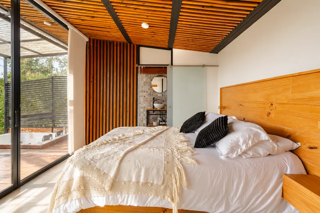 Dormitorio de la cabaña con cama King, techo de madera y ventanales hacia la terraza