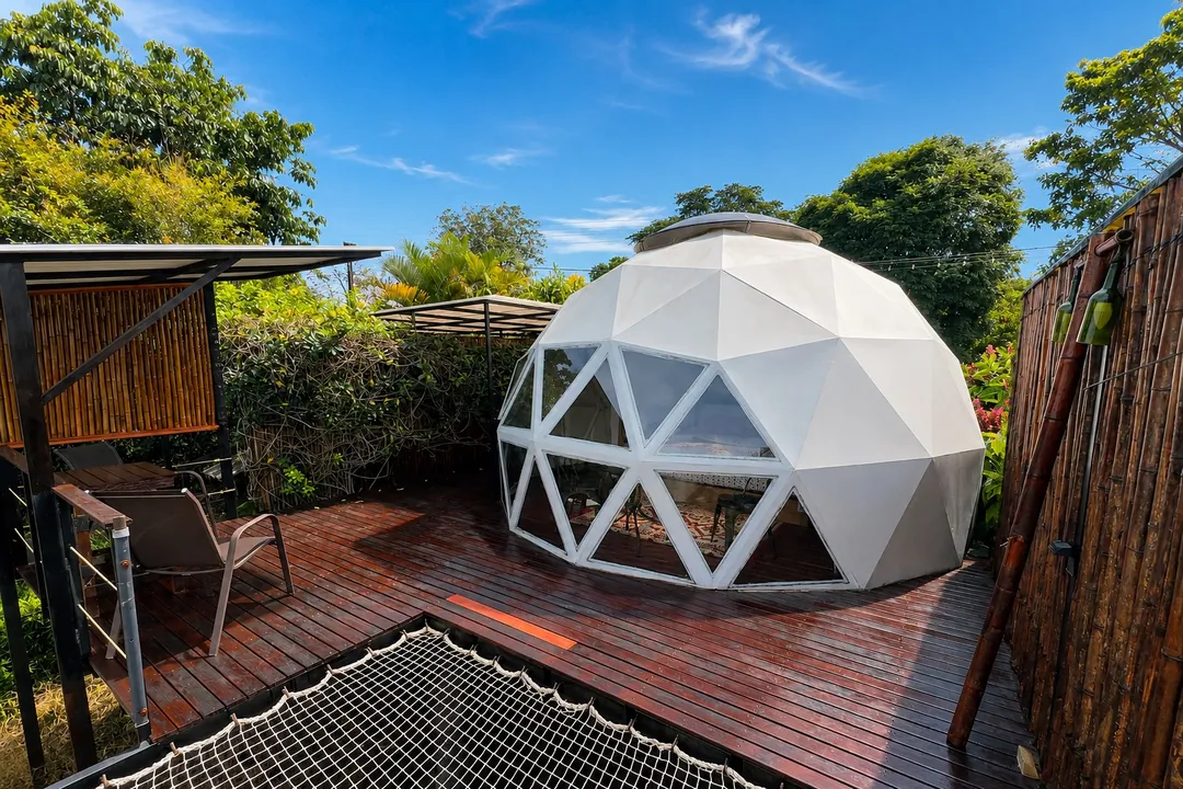 Domo geodésico Ginger sobre su terraza de madera con malla tipo catamarán entre jardines