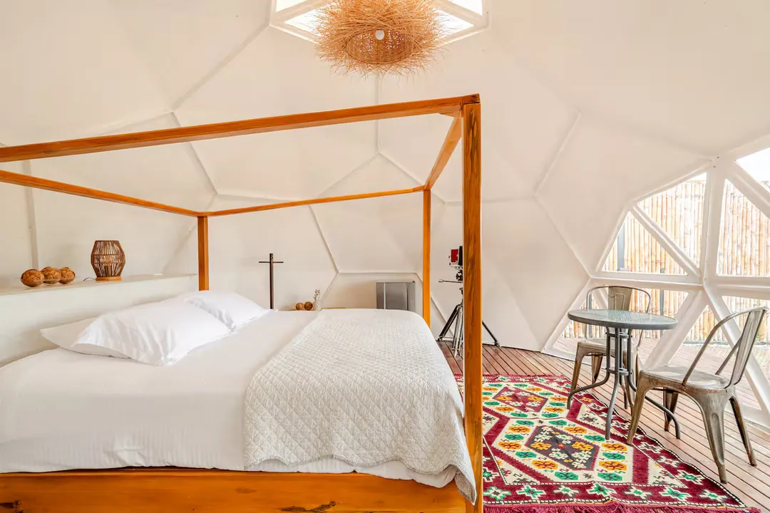 Cama con dosel de madera y lámpara tejida en el interior del domo Ginger